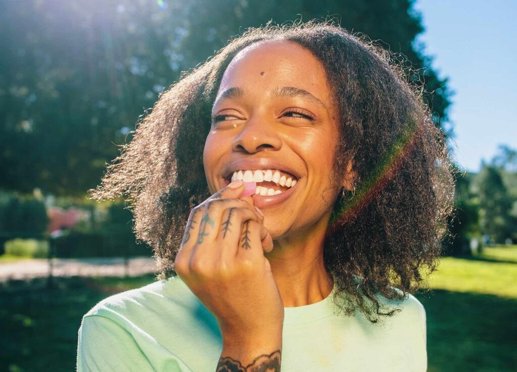 Woman smiling in the sun holding a KANHA Life watermelon hybrid THC gummy to her mouth